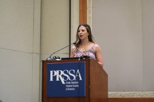 Becca Booker behind a podium with the PRSSA logo